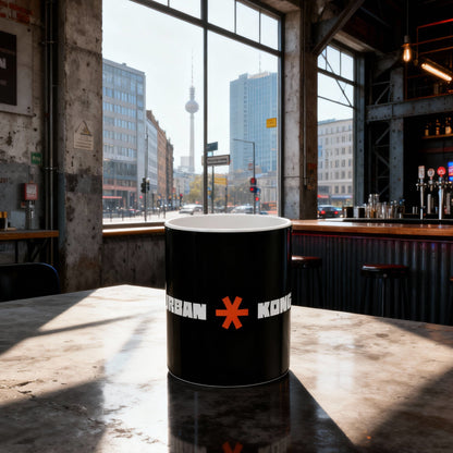 Black cylindrical container with a red logo on a table in an industrial setting with large windows.