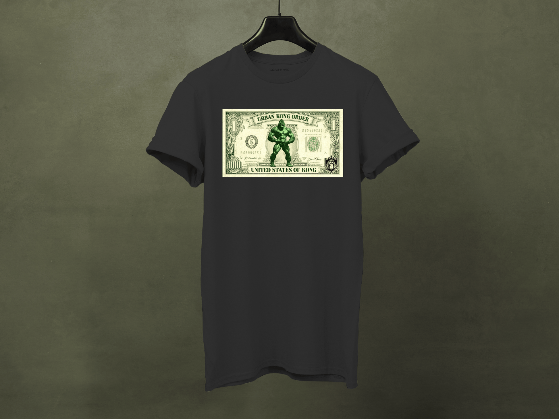 Black t-shirt with a graphic of a superhero on a dollar bill design, hanging against a dark background.