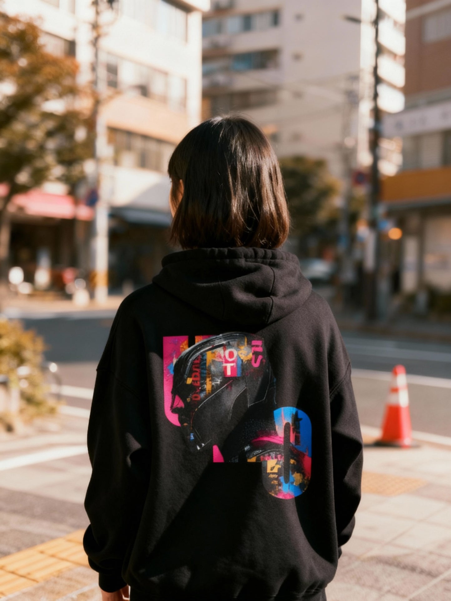 Person wearing a black hoodie with colorful graphics on the back, standing on a street.