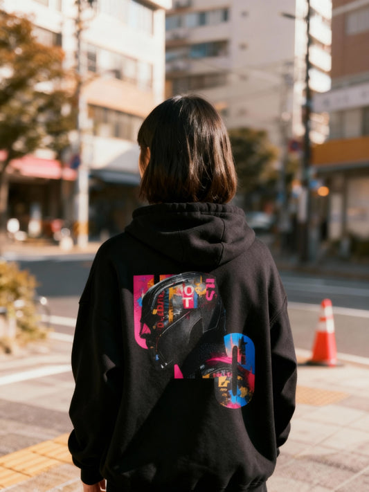 Person wearing a black hoodie with colorful graphics on the back, standing on a street.