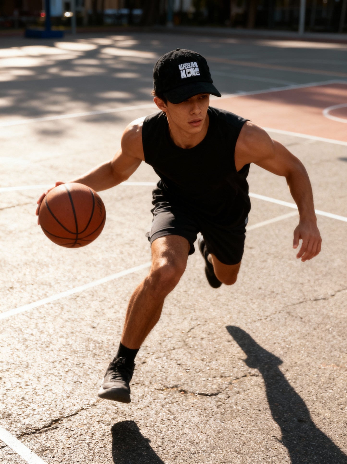 Man playing basketball on an outdoor court wearing a black cap and sleeveless shirt.
