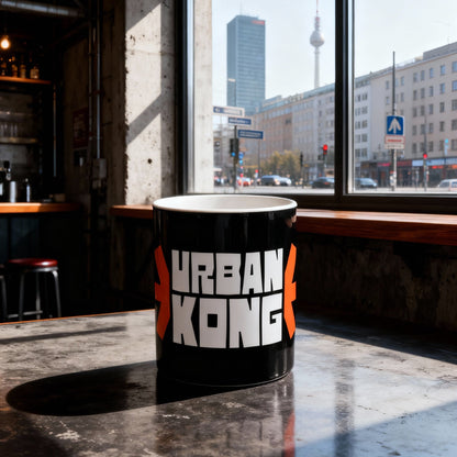 Black mug with 'Urban Kong' branding on a table in a cafe with cityscape view