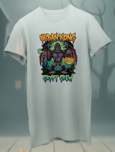 White t-shirt with a colorful graphic design on a Halloween-themed background with pumpkins and a haunted house.